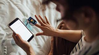 Person reading data on mobile phone while using oximeter to check blood condition.